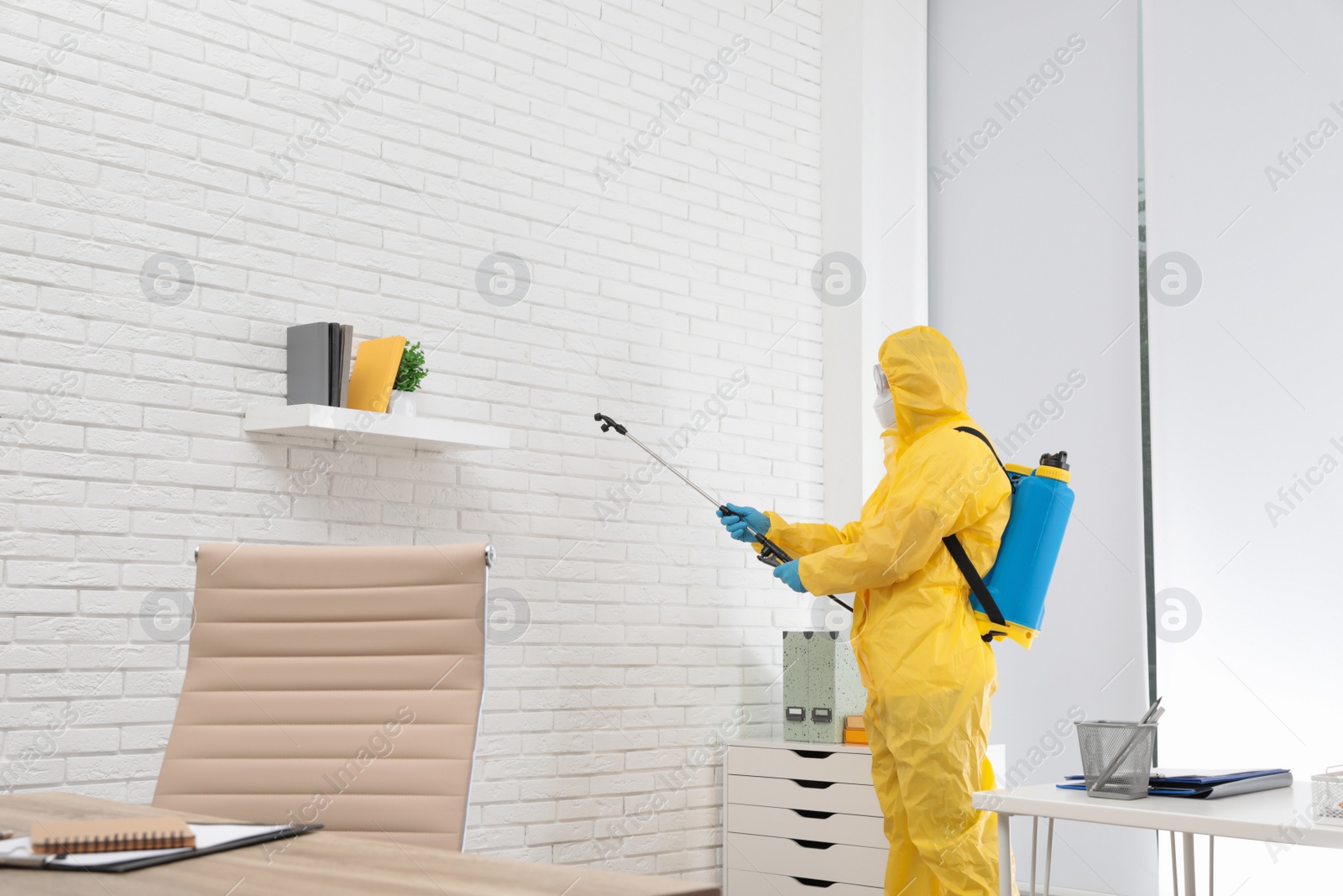 Photo of Janitor in protective suit disinfecting office to prevent spreading of COVID-19