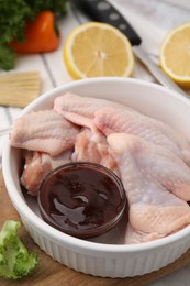 Photo of Fresh marinade, raw chicken wings and other products on rustic wooden table, closeup
