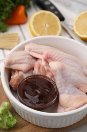 Fresh marinade, raw chicken wings and other products on rustic wooden table, closeup