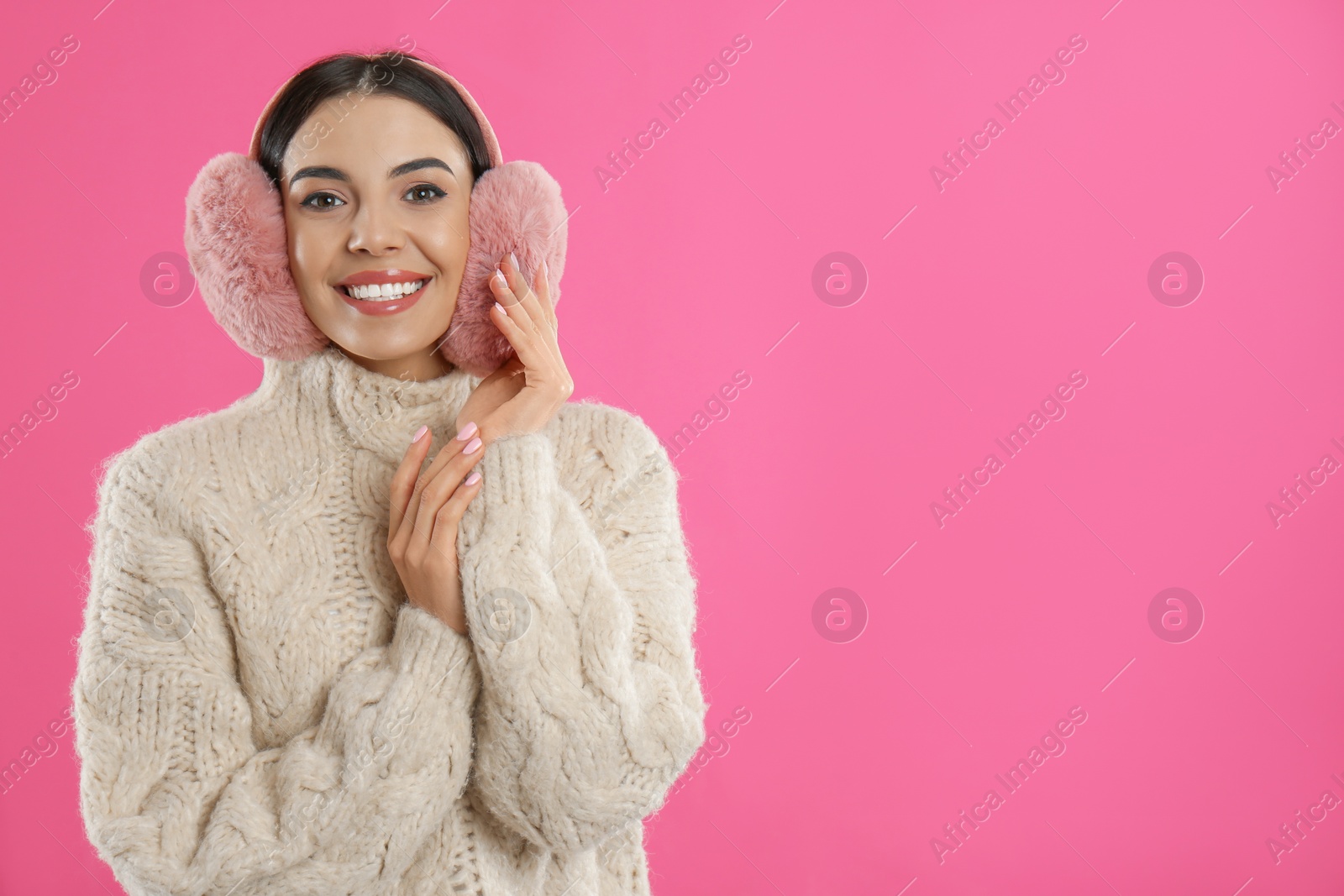 Photo of Beautiful young woman wearing earmuffs on pink background. Space for text