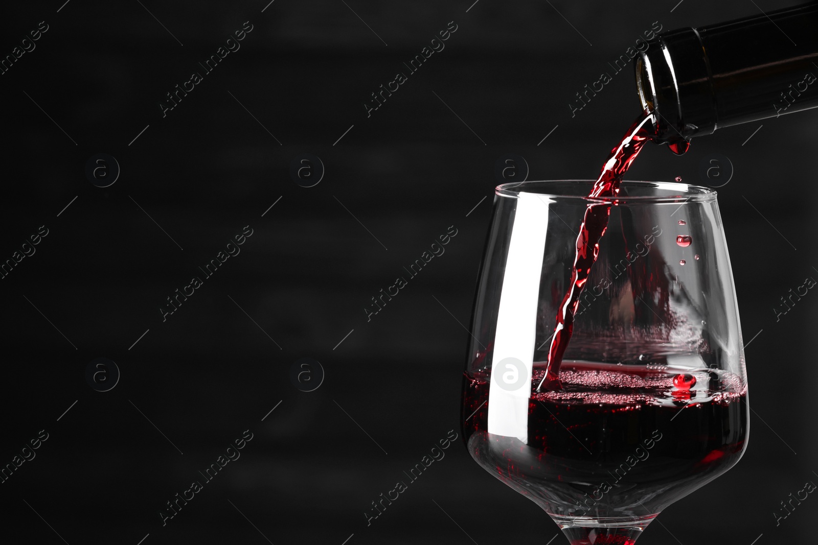 Photo of Pouring red wine into glass against dark background, closeup. Space for text