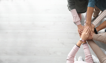Photo of People holding hands together over light wooden background, top view with space for text. Unity concept