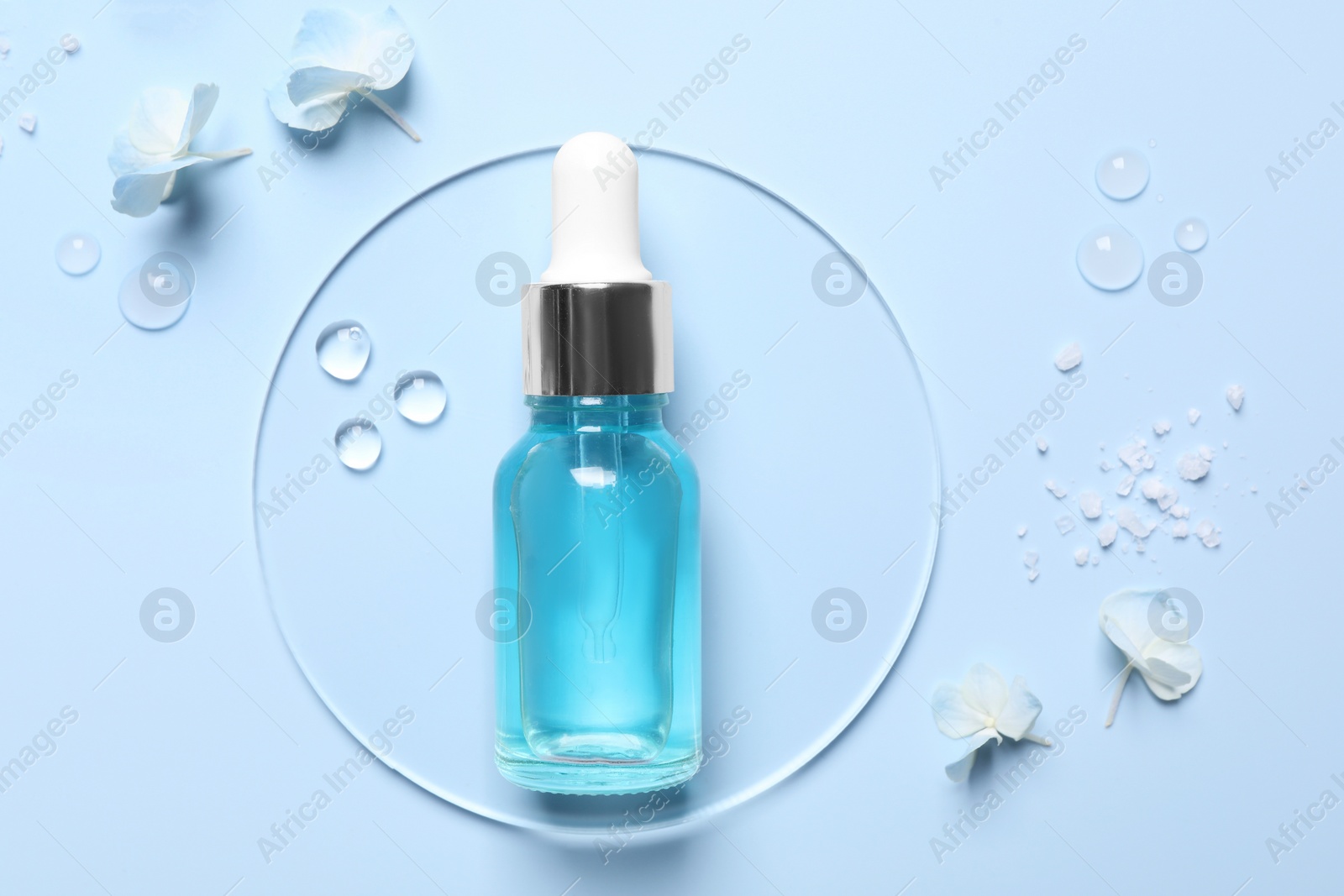 Photo of Bottle of cosmetic serum, flowers and sea salt on light blue background, flat lay