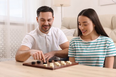Photo of Happy couple playing checkers at table in room