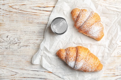 Tasty croissants with sugar powder on wooden background, top view