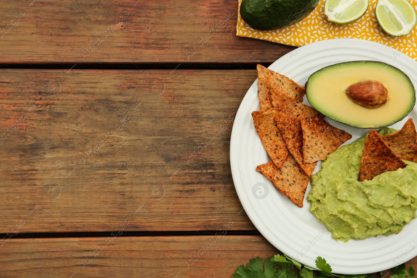 Photo of Delicious guacamole, avocado and nachos on wooden table, flat lay. Space for text