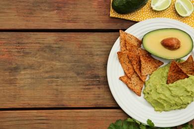 Delicious guacamole, avocado and nachos on wooden table, flat lay. Space for text