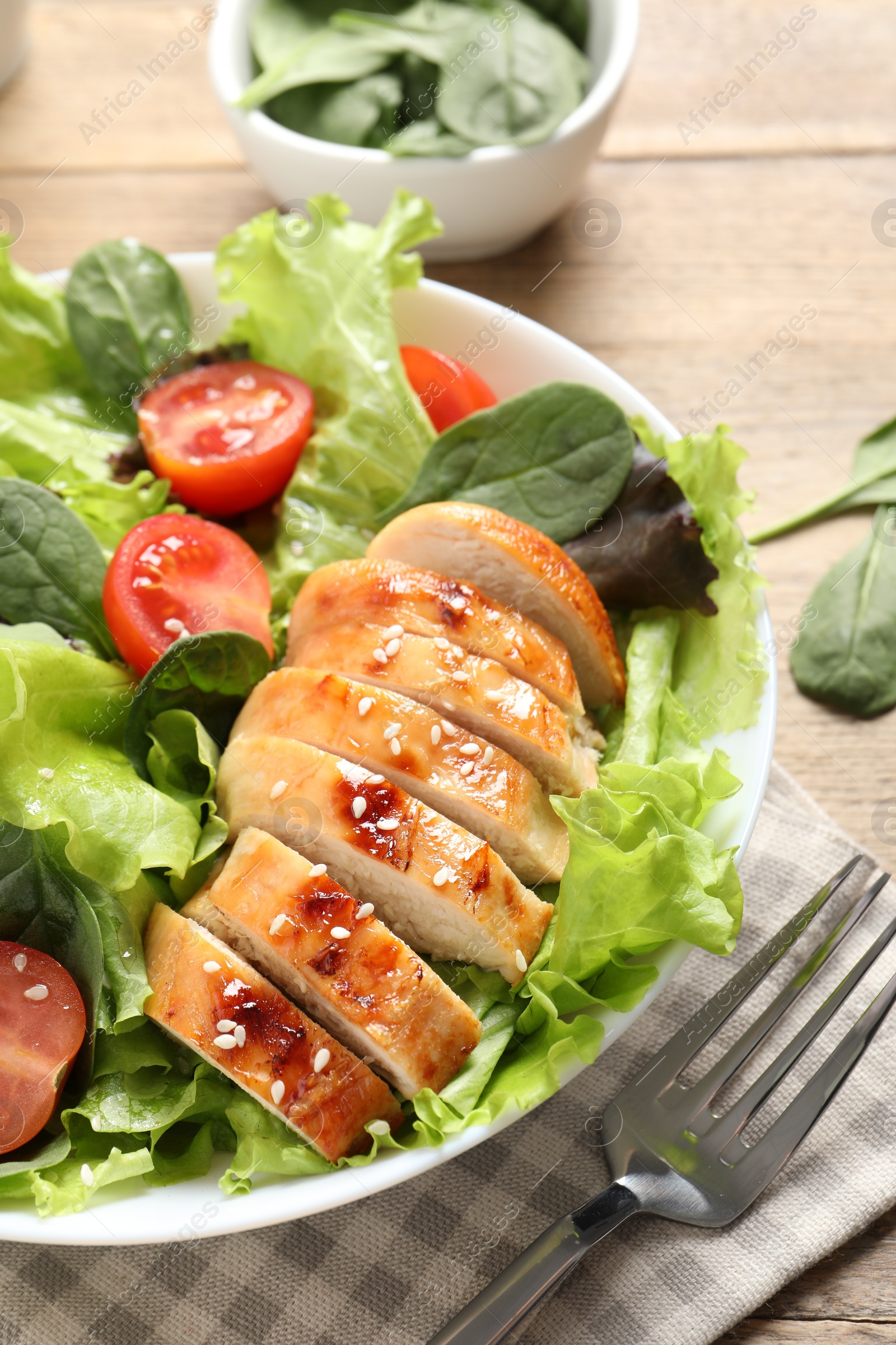 Photo of Eating delicious salad with chicken, cherry tomato and spinach served on table, closeup