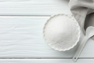 Photo of Granulated sugar in bowl and spoon on white wooden table, top view. Space for text