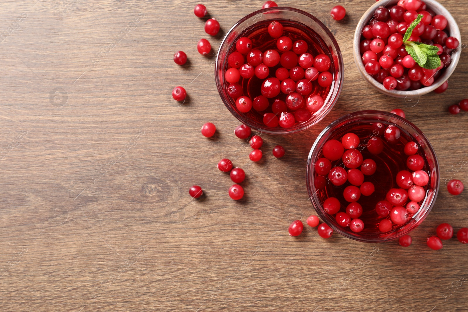 Photo of Tasty cranberry juice in glasses and fresh berries on wooden table, flat lay. Space for text