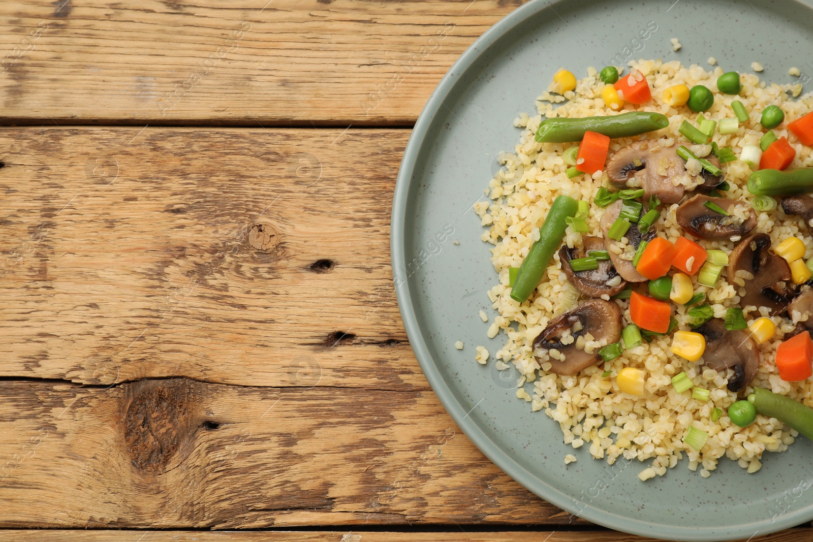 Photo of Delicious bulgur with vegetables and mushrooms on wooden table, top view. Space for text