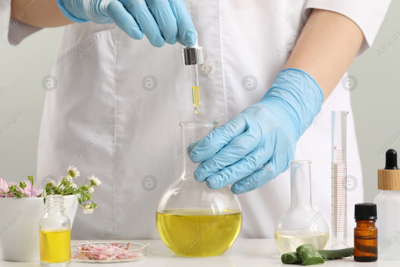 Photo of Scientist developing cosmetic oil at white table, closeup