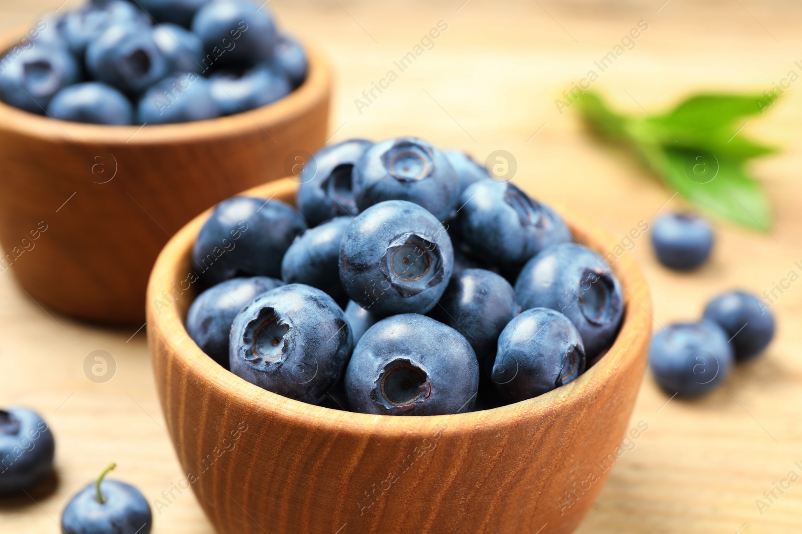 Photo of Bowls of fresh tasty blueberries on wooden table, closeup