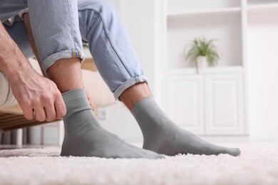 Man putting on grey socks at home, closeup. Space for text