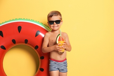 Cute little boy with inflatable ring and glass of cocktail on color background