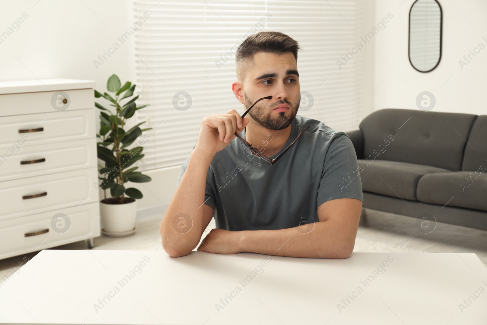Photo of Sad man with glasses sitting at table indoors