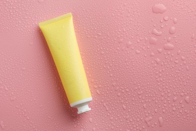 Photo of Moisturizing cream in tube on pink background with water drops, top view. Space for text