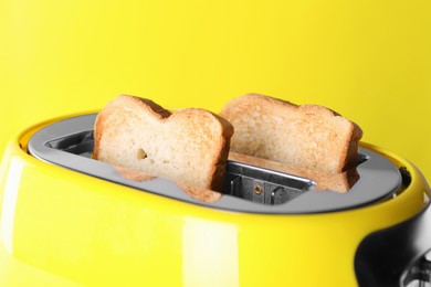 Photo of Modern toaster with slices of roasted bread against yellow background, closeup
