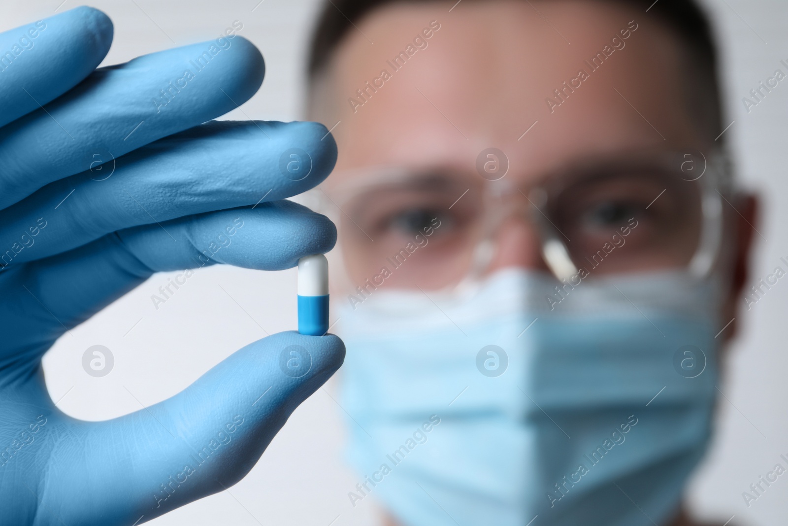 Photo of Doctor holding pill on light background, selective focus. Space for text