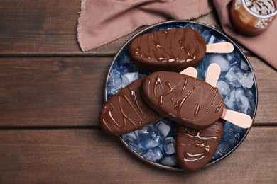 Delicious glazed ice cream bars and ice cubes on wooden table, flat lay. Space for text