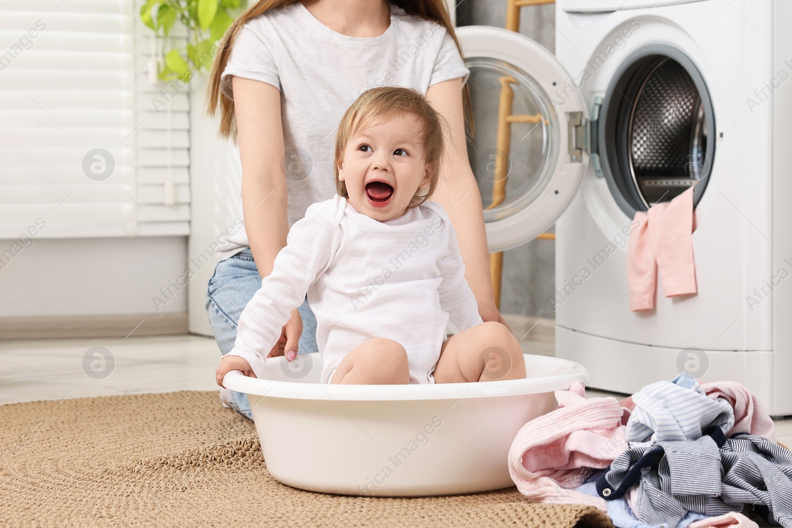 Photo of Happy mother with her daughter having fun while washing baby clothes in bathroom