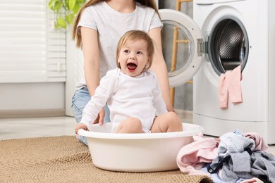 Photo of Happy mother with her daughter having fun while washing baby clothes in bathroom