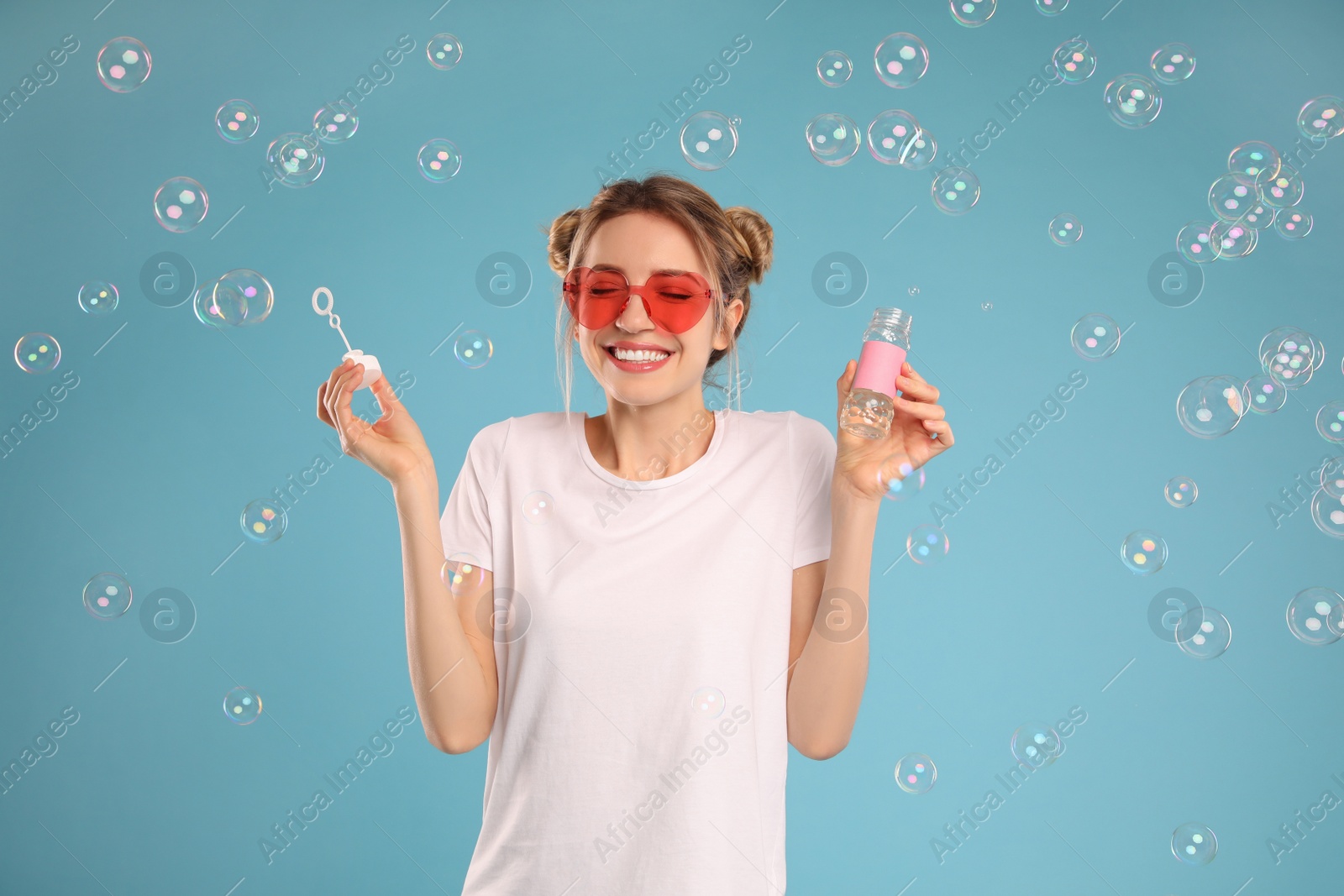 Photo of Young woman blowing soap bubbles on light blue background