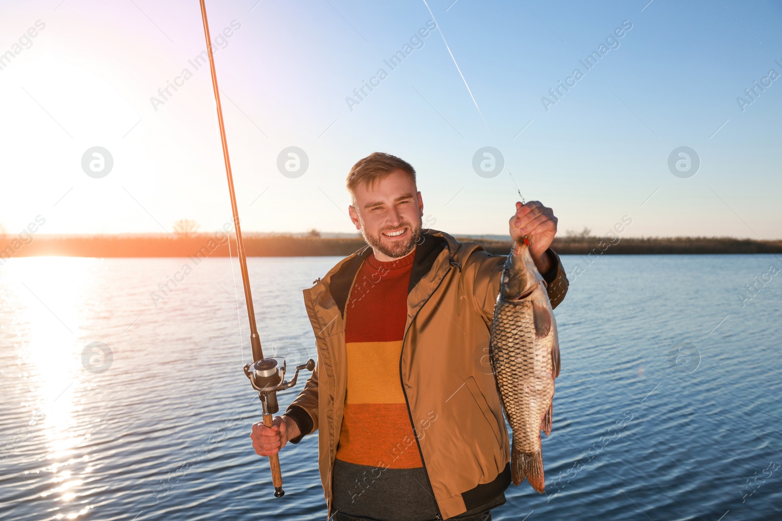 Photo of Fisherman holding fishing rod and catch at riverside