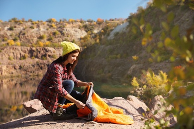 Photo of Young female camper unpacking sleeping bag in wilderness. Space for text