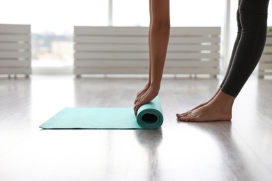 Photo of Woman unrolling mat in yoga studio, closeup