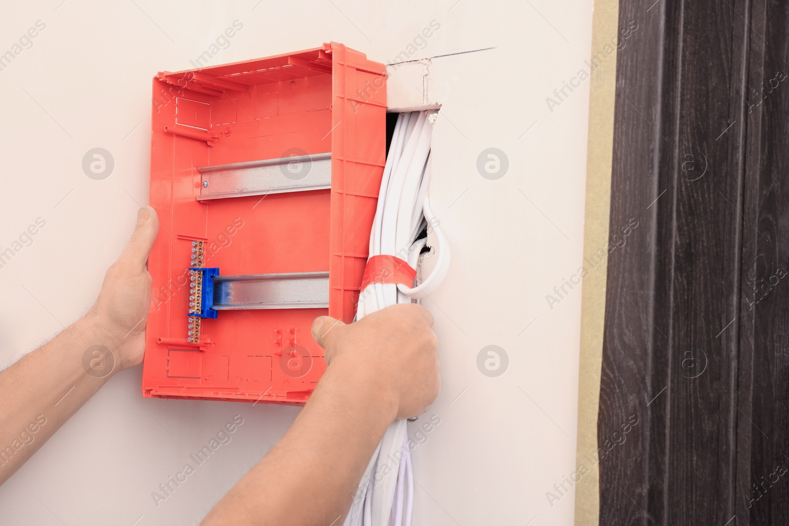 Photo of Electrician with screwdriver installing switchboard on wall indoors, closeup