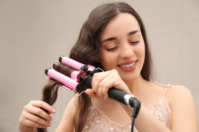 Photo of Young woman using modern curling iron indoors