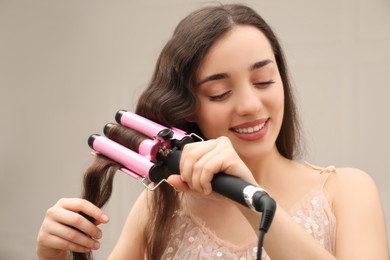 Young woman using modern curling iron indoors