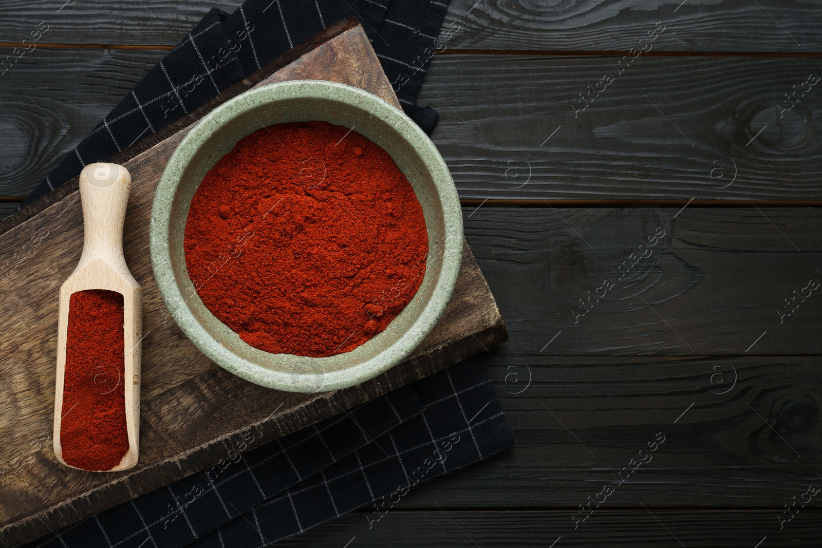 Photo of Bowl and scoop of aromatic paprika on black wooden table, flat lay. Space for text