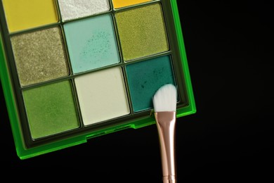 Photo of Colorful eyeshadow palette with brush on black background, above view