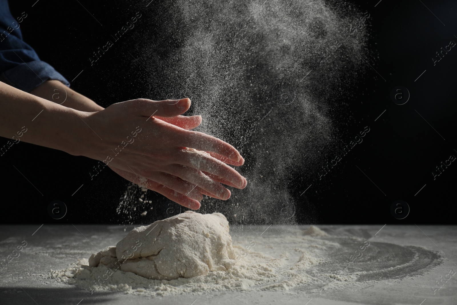 Photo of Making bread. Woman sprinkling flour over dough at table on dark background, closeup. Space for text