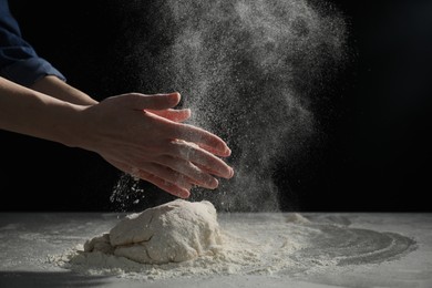 Photo of Making bread. Woman sprinkling flour over dough at table on dark background, closeup. Space for text