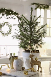 Photo of Small decorated Christmas tree and reindeer figure on table in kitchen
