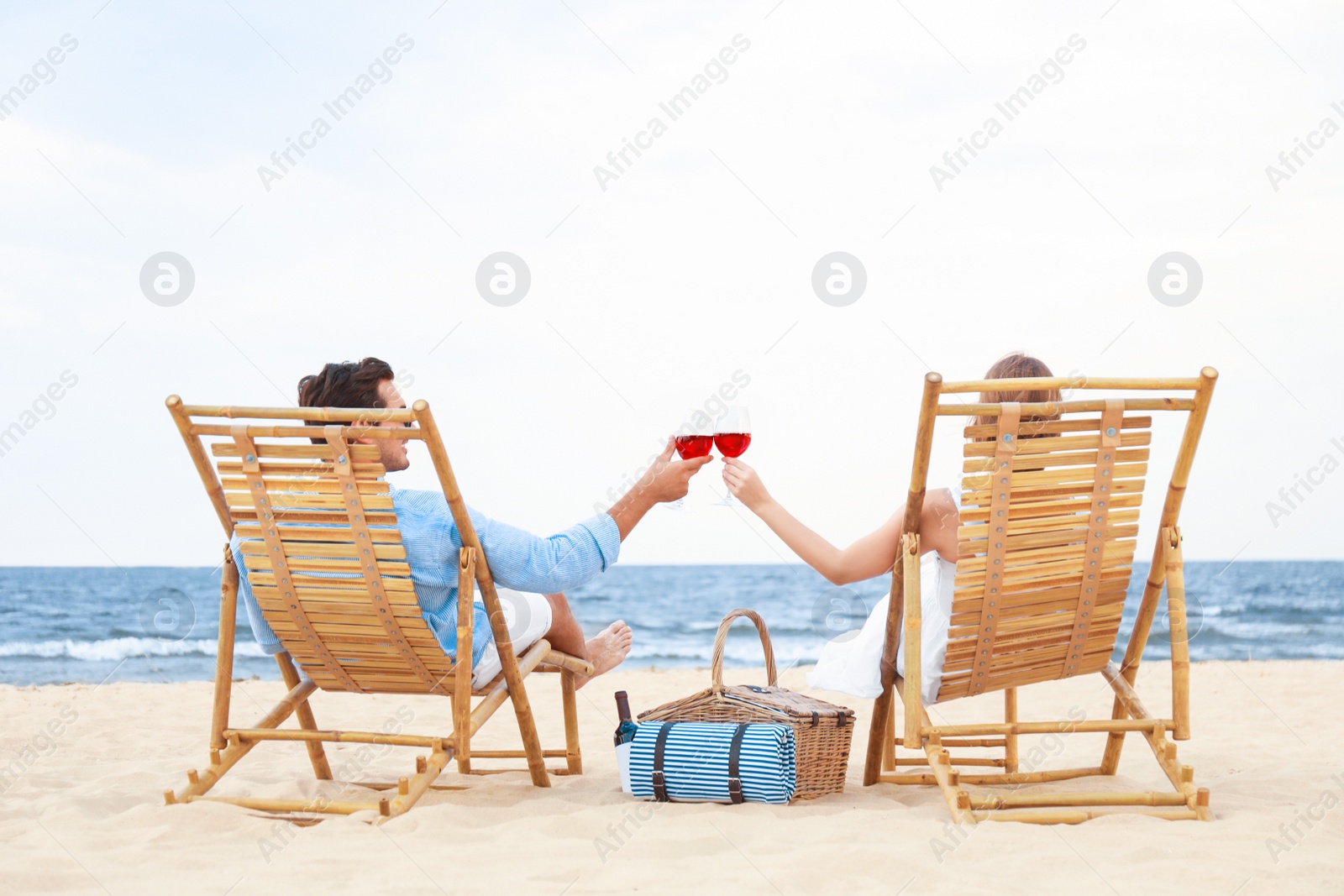 Photo of Happy young couple with glasses of wine sitting on deck chairs at sea beach