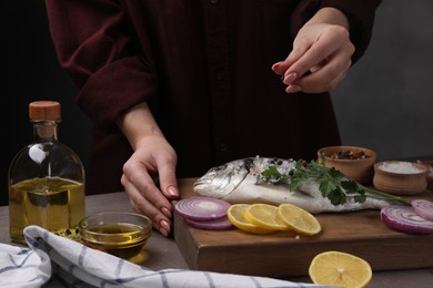 Woman adding spices onto raw dorado fish at grey table, closeup