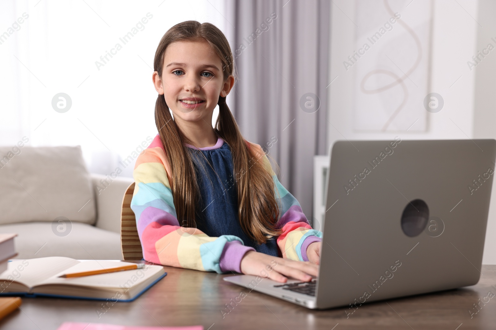 Photo of E-learning. Cute girl using laptop during online lesson at table indoors