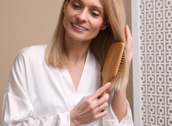 Photo of Beautiful woman in white robe brushing her hair indoors