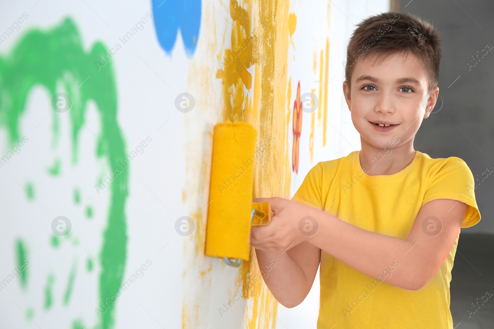 Photo of Little child painting wall with roller brush indoors