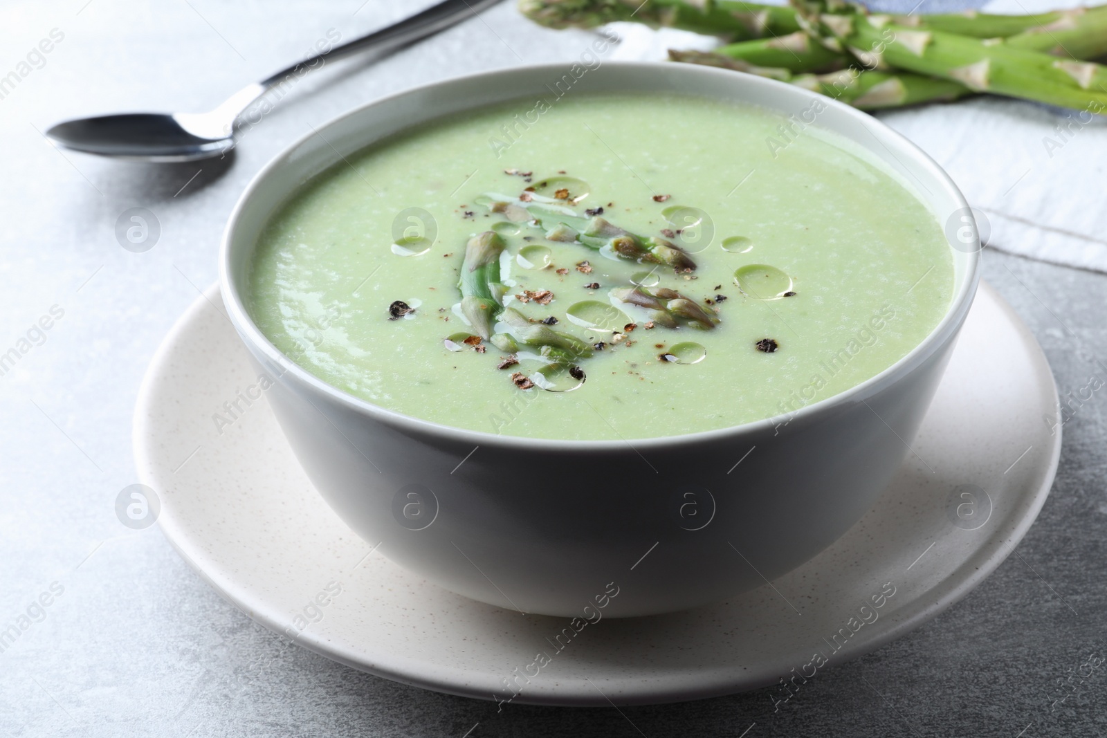 Photo of Delicious asparagus soup served on light grey table, closeup