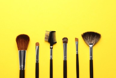 Photo of Set of makeup brushes on yellow background, flat lay. Space for text