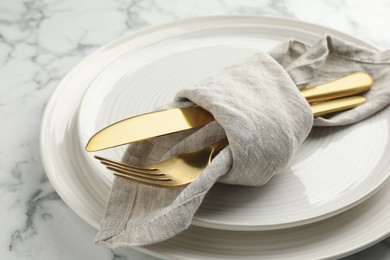 Photo of Stylish setting with cutlery, napkin and plates on white marble table, closeup
