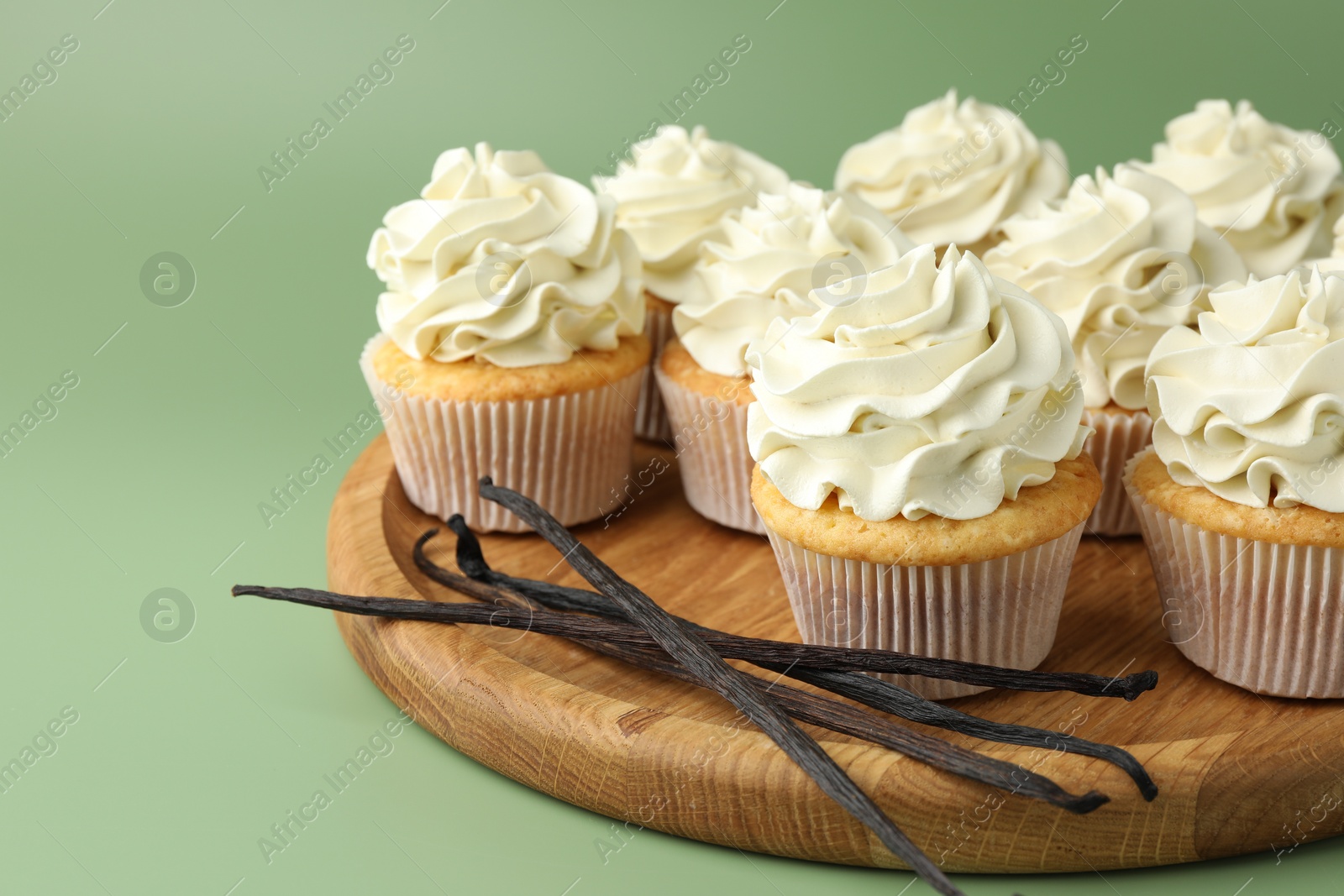 Photo of Tasty cupcakes with cream and vanilla pods on green background