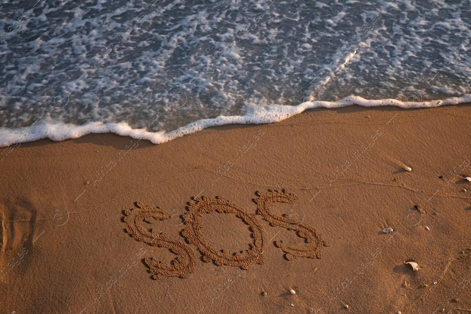 Image of SOS message drawn on sandy beach near sea, above view