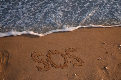 SOS message drawn on sandy beach near sea, above view