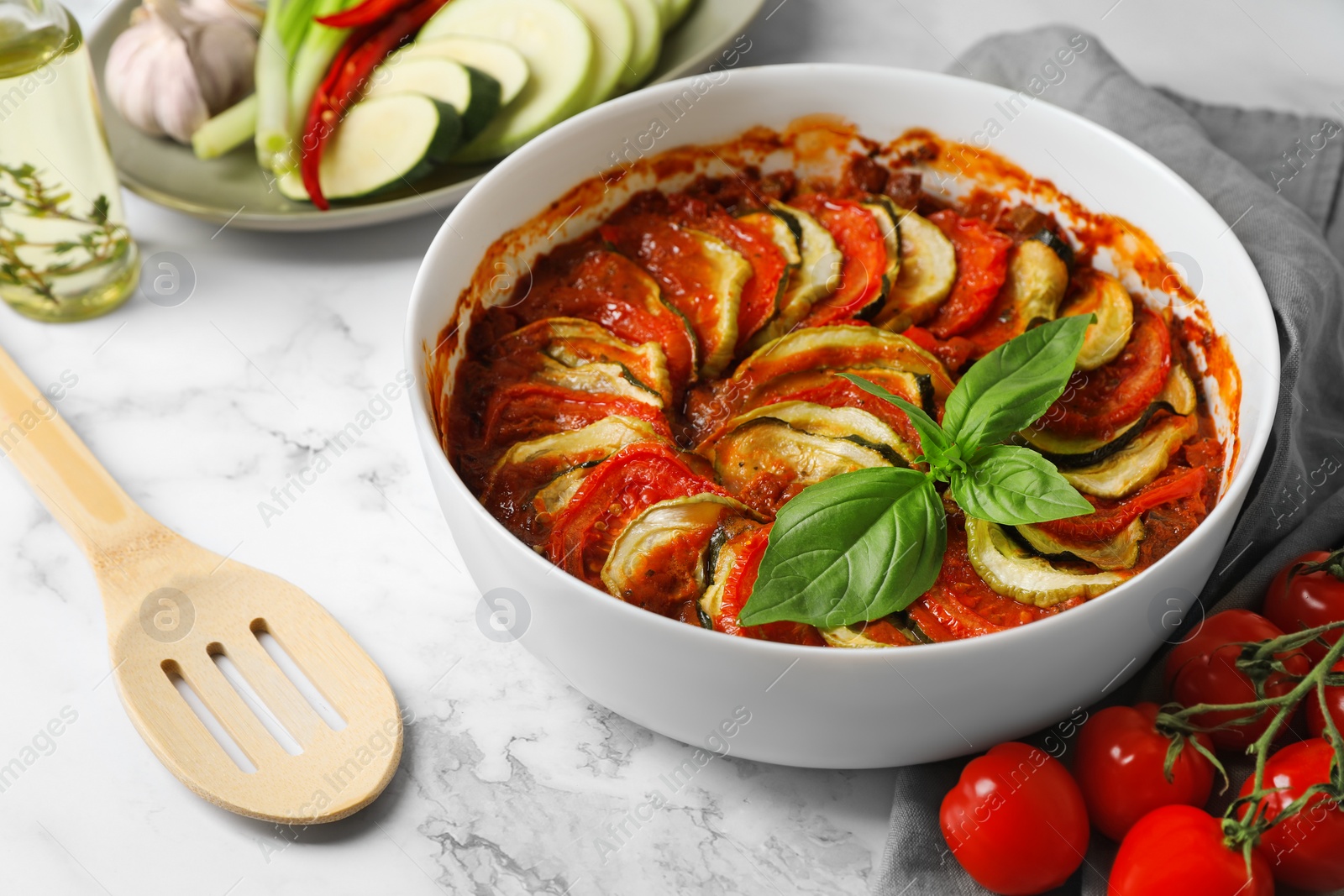 Photo of Delicious ratatouille and ingredients on white marble table